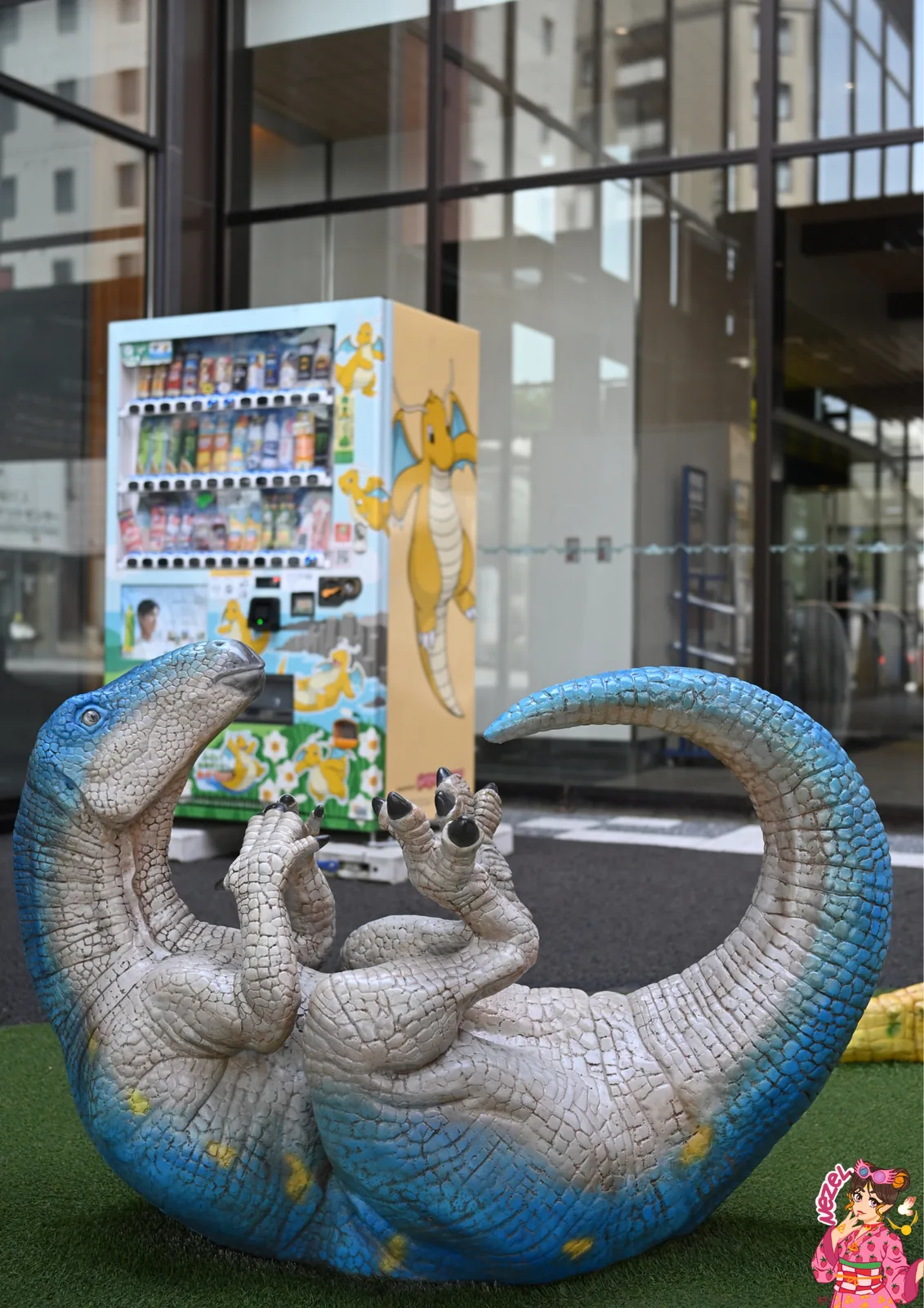 Statue d'un dinosaure au long cou &agrave; c&ocirc;t&eacute; d'un distributeur aux couleurs de Dracolosse