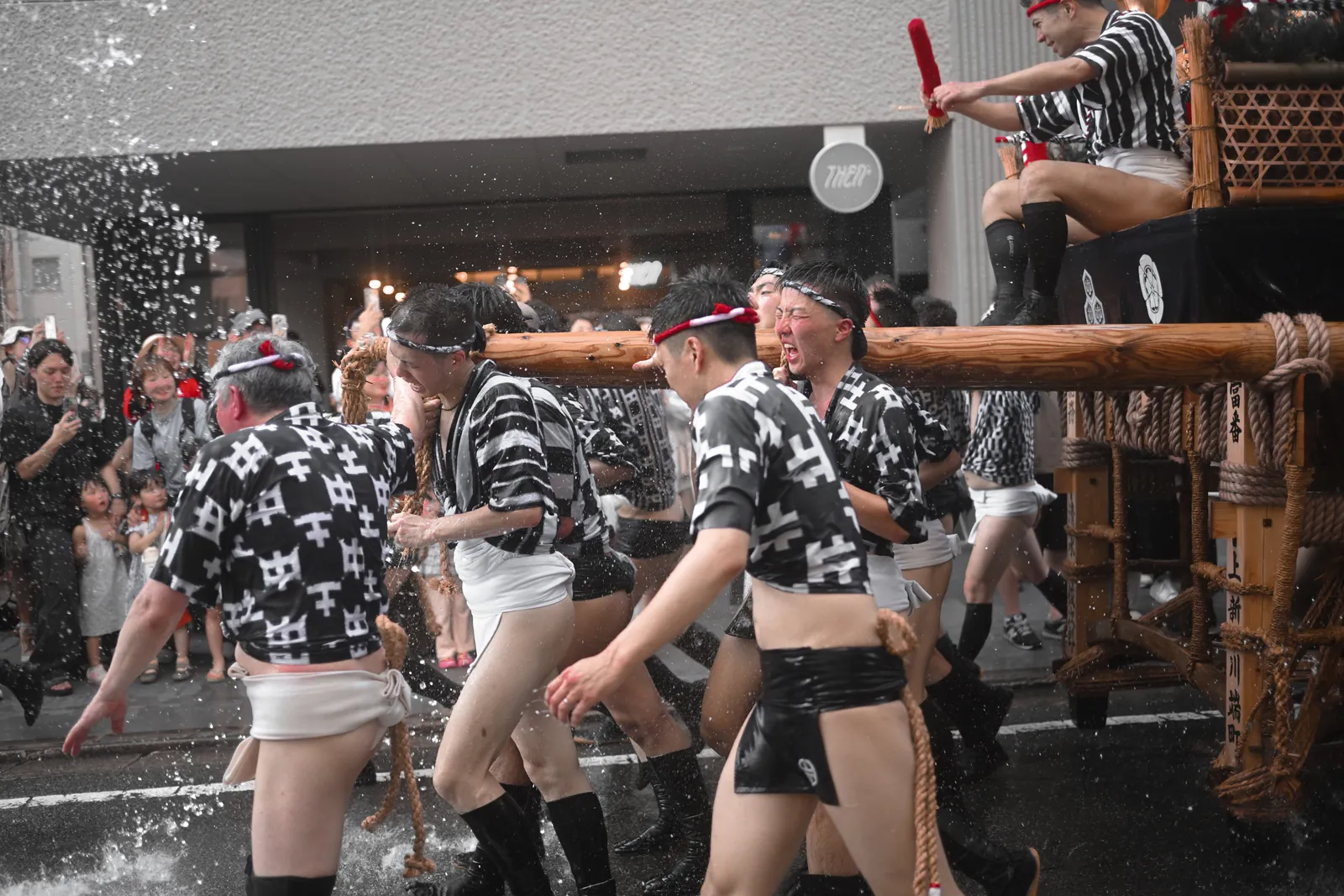 Porteurs d'un char Kakiyama recevant de l'eau en pleine course, dans une rue de Hakata