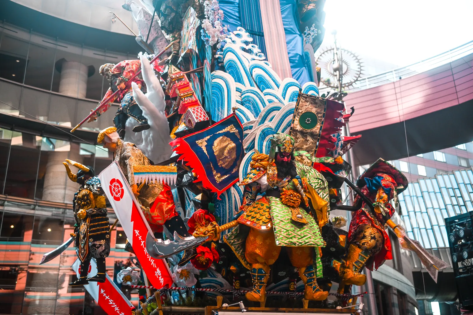 Char décoratif Kazariyama du Hakata Gion Yamakasa, orné de guerriers et de vagues bleues, installé sous une verrière