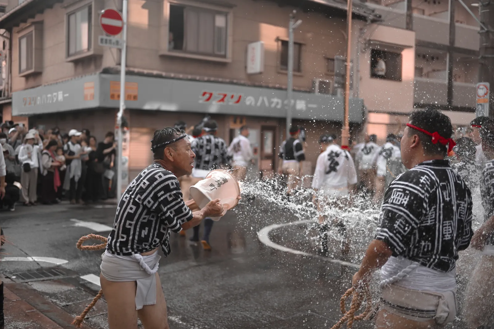Spectateur lançant un seau d'eau sur les porteurs pendant une course du Hakata Gion Yamakasa