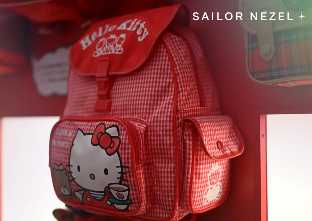 Sac à dos d'enfant en vichy rouge et blanc, avec un rabat marqué Hello Kitty et une poche illustrée du personnage tenant une tasse