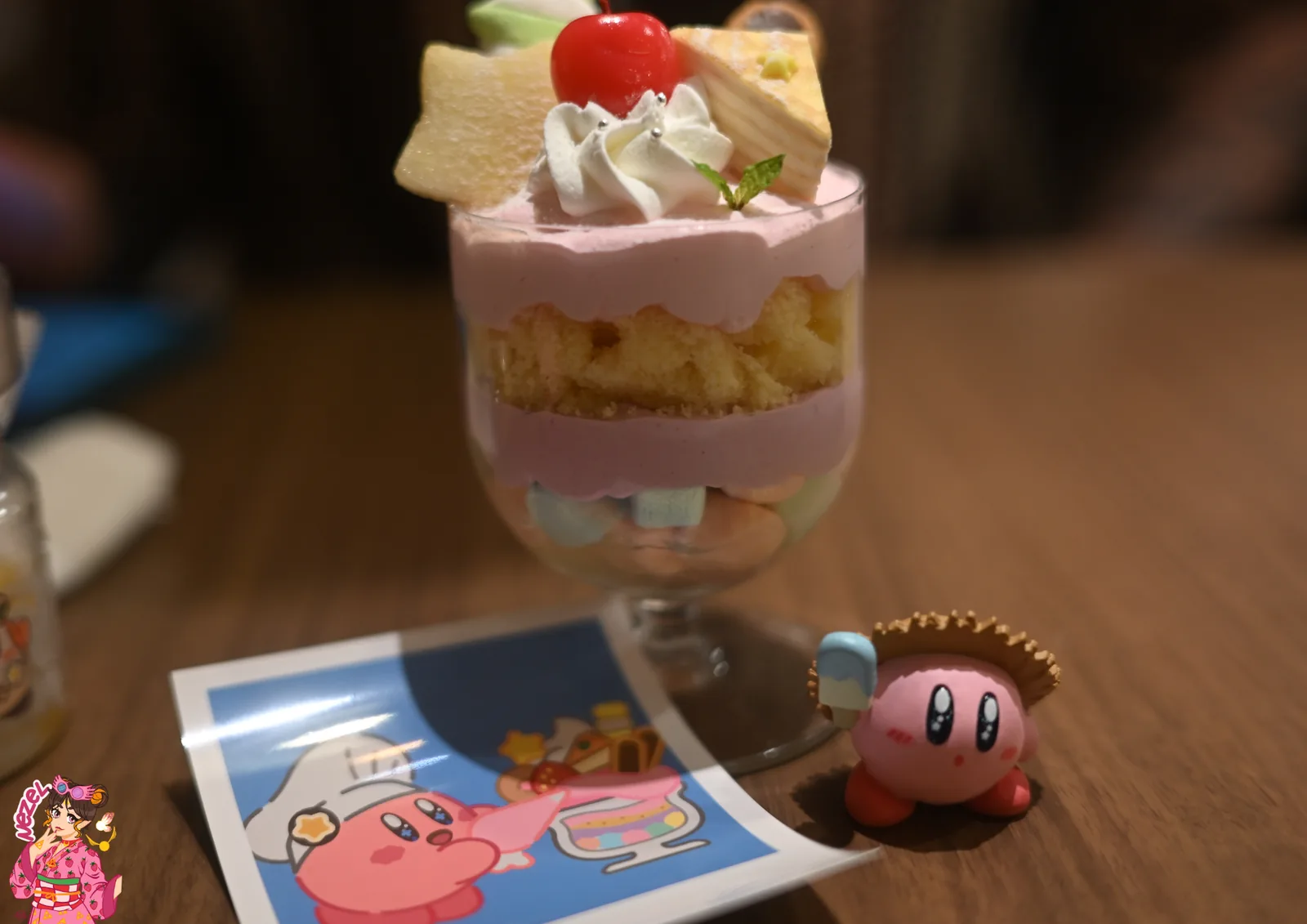 Parfait rose du Kirby Café en verre, servi avec une figurine Kirby et la photo souvenir offerte